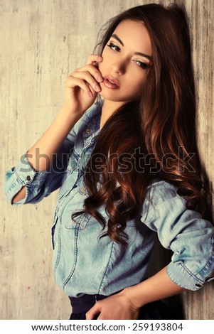 Beautiful sensual woman in jeans clothes stands by the grunge wall. Fashion.