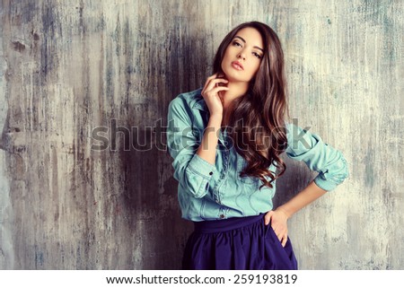 Beautiful sensual woman in jeans clothes stands by the grunge wall. Fashion.