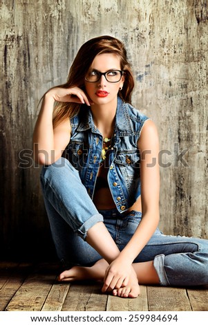 Pretty girl in casual jeans clothes sitting on a wooden floor by the grunge wall. Fashion.
