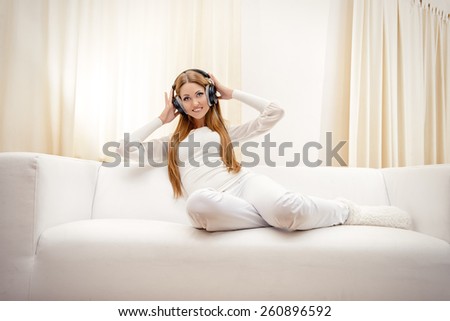 Happy young woman resting at home listening to music in headphones.
