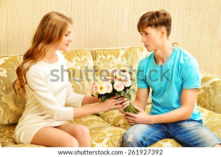 Young man giving flowers to his sweetheart. They are in the cozy living room. Family, love concept.