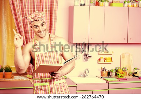 Handsome muscular man in an apron studies a cookbook in the pink kitchen. Love concept. Valentine\'s day. Women\'s day.