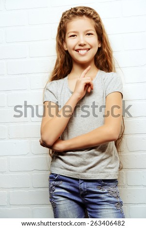 Joyful teen girl in casual clothes stands by the brick wall. Active lifestyle. Studio shot.