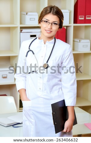 Portrait of a kind woman doctor standing in her consulting room with a stethoscope and smiling at the camera. Healthcare, medicine.
