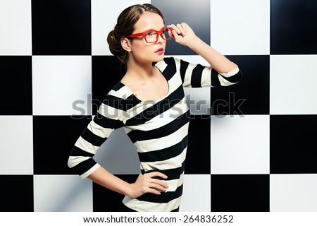 Fashion shot of an elegant model in glasses posing in dress in black and white stripes on a background of black and white squares. Beauty, fashion concept. Business style.