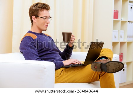 Portrait of a goodlooking smiling young man sitting on a couch at home and working on his laptop.