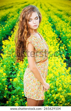 Beautiful girl standing in a field of blooming yellow flowers. Summer.