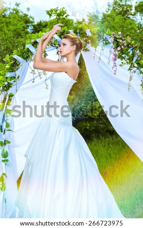 Beautiful elegant bride stands under the wedding arch. Wedding dress and accessories. Wedding decoration.