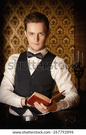 Handsome well-dressed man stands by the fireplace in a room with classic interior. Fashion.