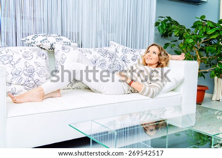 Smiling elegant woman lying on a sofa in a living room. Home interior, furniture. Lifestyle.