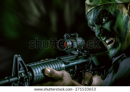 A soldier in war paint looks through the scope of automatic rifles. Military, war. Special forces.
