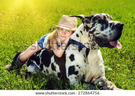 Happy little girl with her mastiff dog on a meadow in summer day. Countryside.