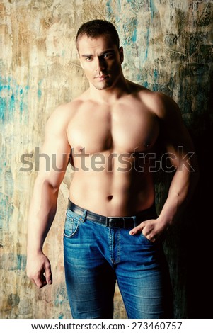 Portrait of a handsome muscular man full of strength standing by a grunge wall. Jeans style.