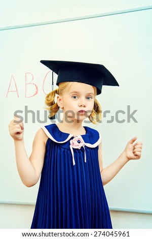 Cute little student girl in academic hat during the lesson at school. Educational concept.