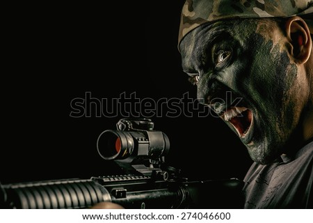 A soldier in war paint looks through the scope of automatic rifles. Military, war. Special forces.