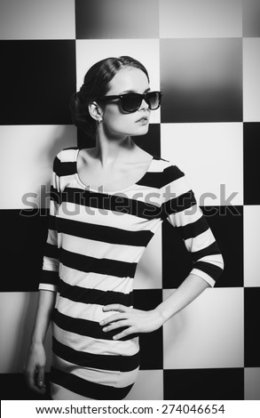 Beautiful fashion model posing in dress in black and white stripes on a background of black and white squares. Beauty, fashion concept. Black-and-white photo.