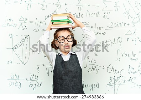 Funny smart schoolgirl in big glasses stands with books at the blackboard. Education.