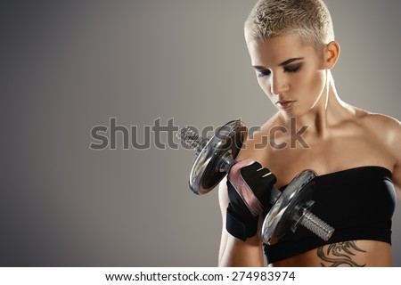 Muscular young woman with beautiful athletic body doing exercises with dumbbells. Fitness, bodybuilding. Health care.