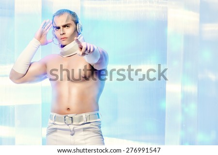 Technologies of the future, man of the future. Handsome muscular man with futuristic make-up in the headphones standing on a luminous transparent background and touches the screen with his finger.