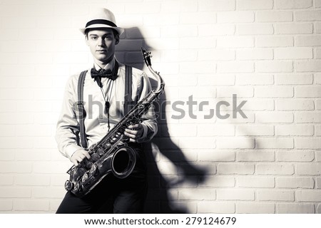 Black-and-white portrait of an elegant musician standing with his saxophone by the brick wall. Art and music. Jazz music.