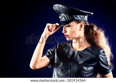 Sexual young woman alluring in fitting leather suit and a cap of police officer. Beauty, fashion.