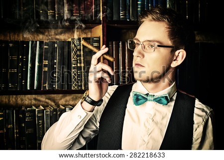 Young handsome man in evening suit stands by the fireplace in a room with classic vintage interior. Fashion.