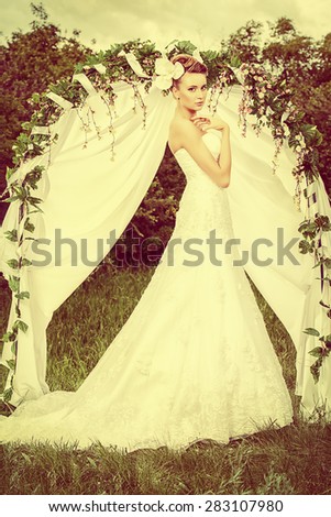 Beautiful elegant bride stands under the wedding arch. Wedding dress and accessories. Wedding decoration.
