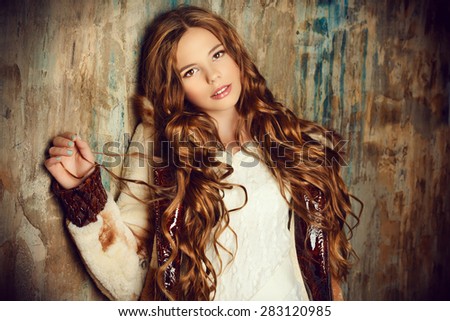 Fashion shot of a pretty teenager girl with beautiful long curly hair wearing fur coat. Beauty, fashion.