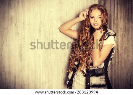 Fashion shot of a pretty teenager girl with beautiful long curly hair wearing white knitted dress and fur jacket. Beauty, fashion.