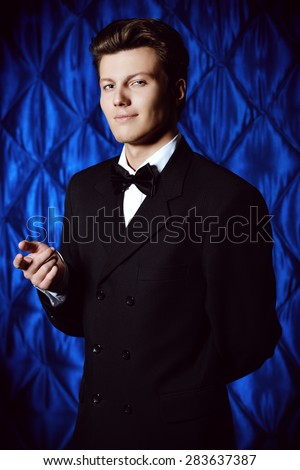 Portrait of a handsome young man in black suit over vintage background smiling at camera. Fashion, style.