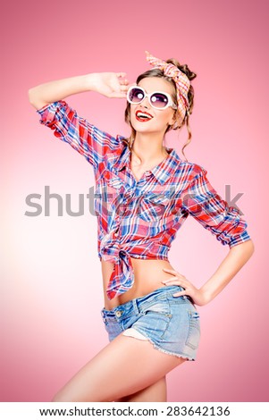 Pretty pin-up girl alluring in shorts and shirt over pink background. Beauty, fashion. Optics, eyewear.