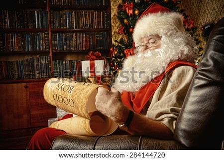 Santa Claus dressed in his home clothes sitting in the room by the fireplace and Christmas tree. He is reading a list of good boys and girls. Christmas. Decoration.