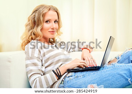 Smiling elegant woman sitting on a sofa with her laptop computer. Home interior, furniture. Lifestyle.