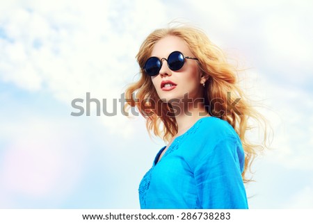 Gorgeous young woman with beautiful wavy hair wearing casual blouse and sunglasses posing outdoor. Fashion shot.