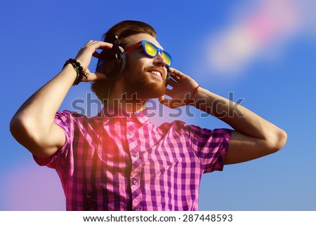 Portrait of a dreamy handsome young man listening to music in headphones. Blue sky background. Leisure, summer, vacation.