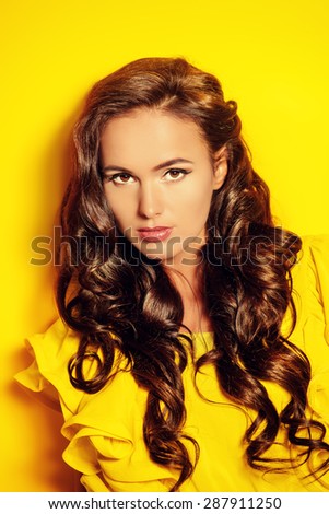 Beautiful summer girl in yellow dress looking at camera, over yellow background. Beauty, fashion.