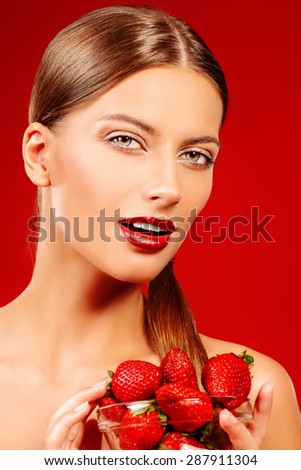 Attractive young woman eating fresh strawberry. Sexual lips, red lipstick. Healthy food concept. Red background.
