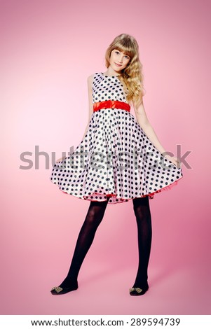 Full length portrait of a pretty teenager girl posing in pin-up dress over pink background.