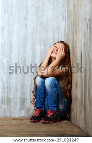 Portrait of a sad girl child sitting in the corner of the room. Loneliness, depression. Awkward age.