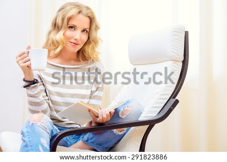 Beautiful young woman resting at home in a cozy armchair with a cup of tea. Interior.