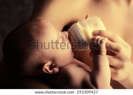 Caring father feeding his baby from a bottle. Healthy baby food and infant formula, milk. Studio shot over black background.