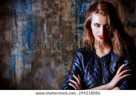 Gorgeous young woman wearing black leather jacket posing by the grunge wall. Beauty, fashion concept.