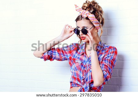 Pretty pin-up girl alluring by the brick wall in shorts and shirt. Beauty, fashion. Optics, eyewear.