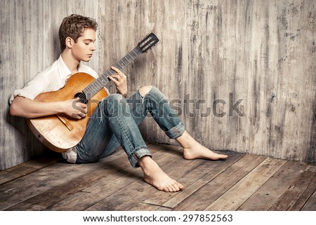Romantic young man playing an acoustic guitar, sitting on the wooden floor