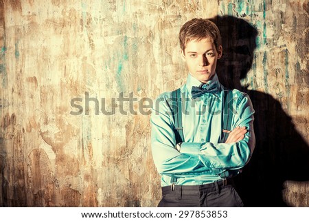 Elegant young man stands by the grunge wall and looking to camera. Men\'s beauty, fashion. Business.