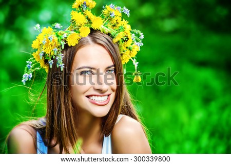 Romantic smiling girl in a wreath of wild flowers sitting on the lawn. Summer life. Beauty.
