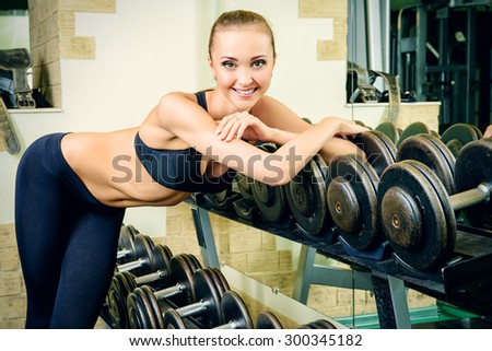 Beautiful young woman with perfect figure is training with dumbbells at the gym. Active lifestyle, bodycare. Fitness equipment.