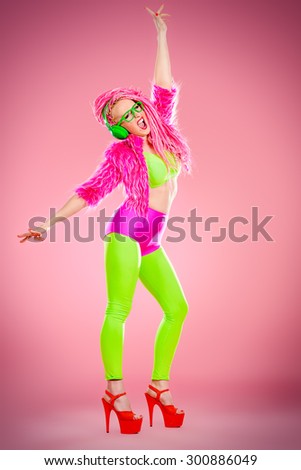 Full length portrait of a dancing glamorous show girl in bright clothes, headphones and with bright pink dreadlocks. Disco, party. Show business. Bright fashion.