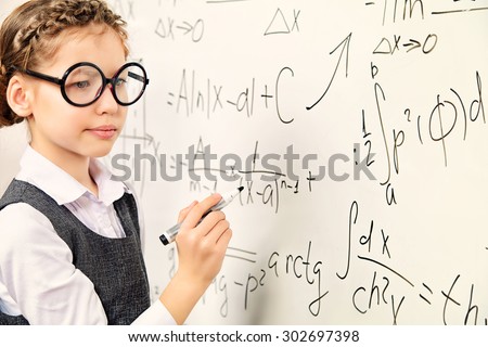 Happy smart schoolgirl in big glasses performs the task at the blackboard. Education.