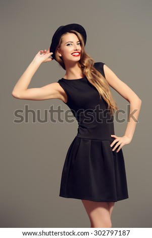 Joyful pretty girl wearing black dress and black classic hat smiling at camera. Beauty, fashion concept. Hipster style.